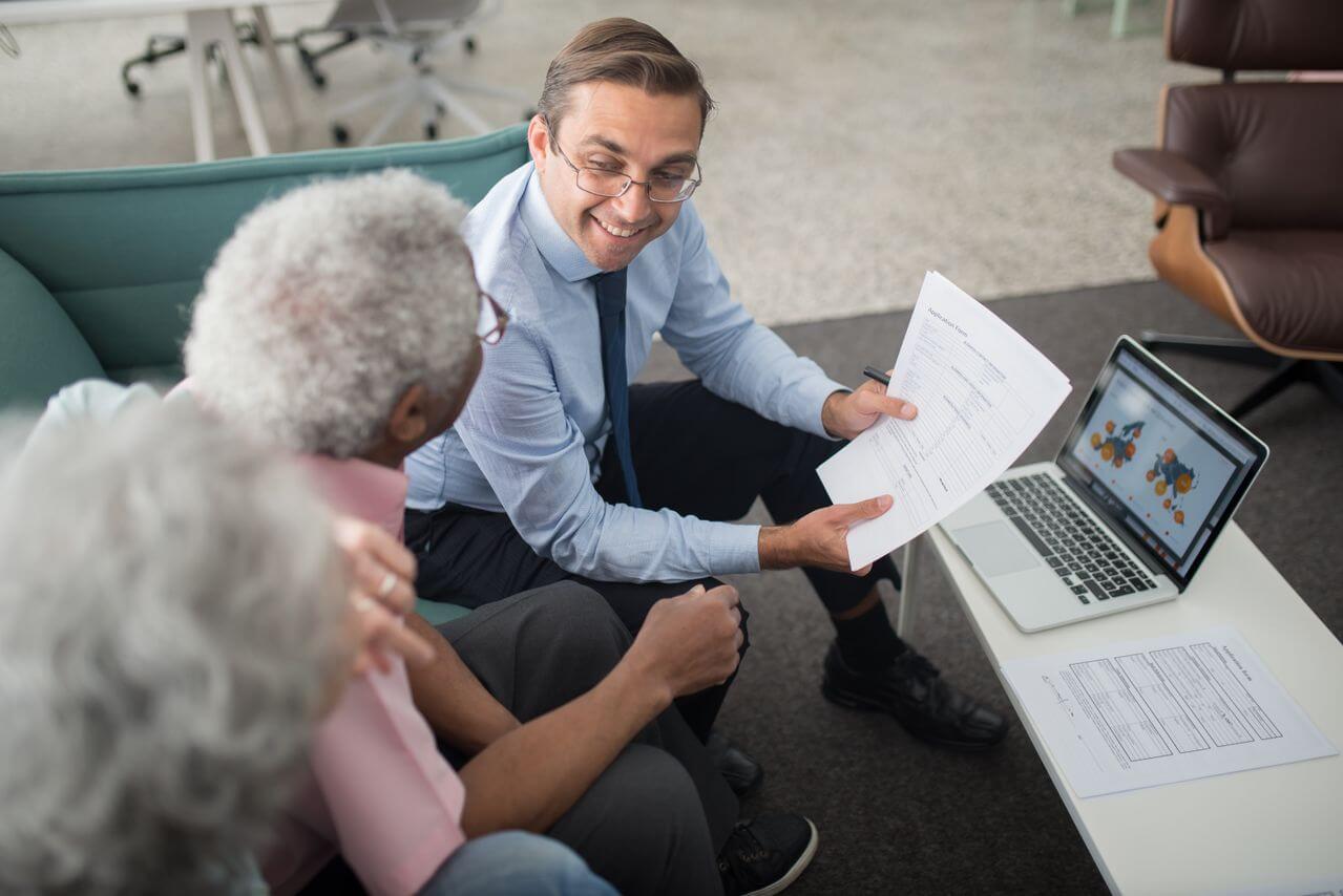 Precious metals specialist showing physical gold IRA rollover documents to an elderly couple
