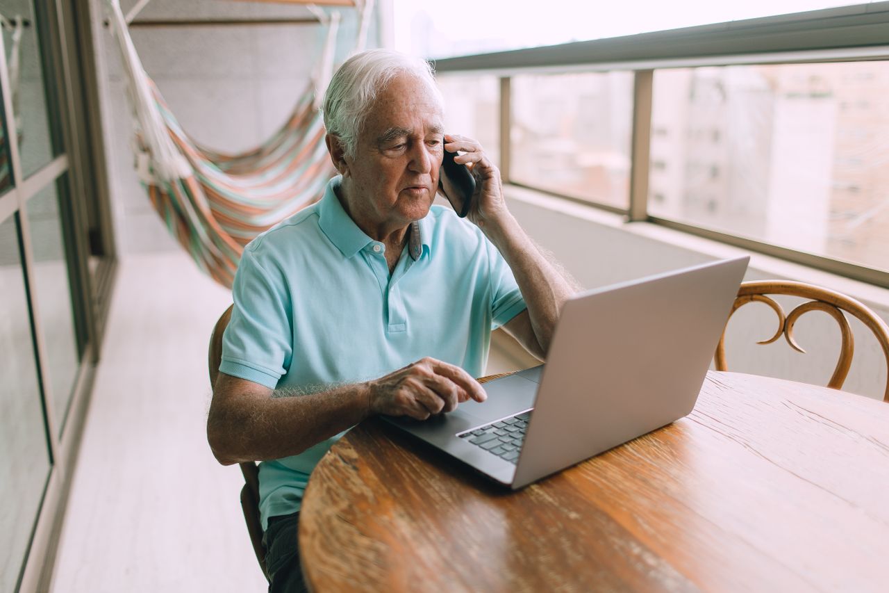Elderly man looking at laptop and talking on phone about retirement account options